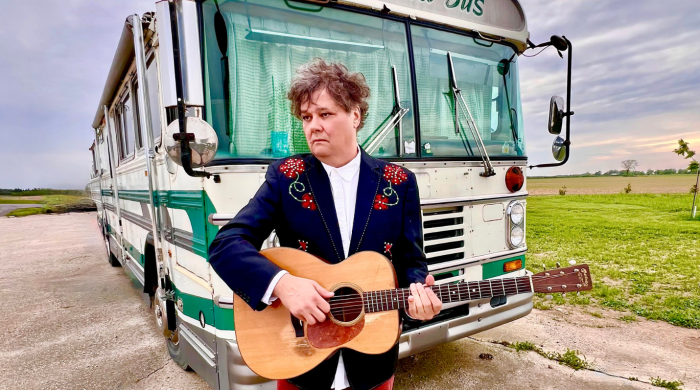 Artist Ron Sexsmith standing in front of old school bus with guitar
